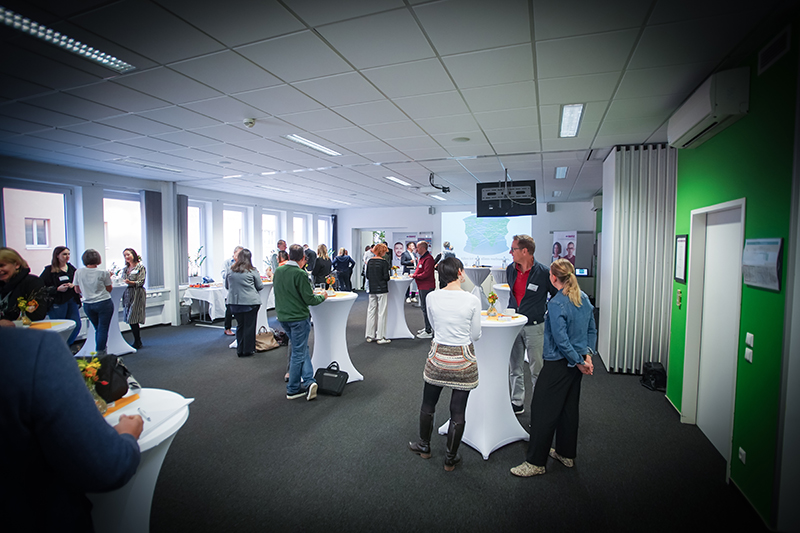 Einblick in ein Firmenfr&uuml;hst&uuml;ck. Personen stehen an Stehtischen und unterhalten sich