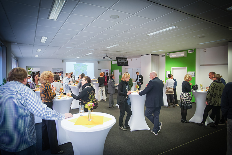 Einblick in ein Firmenfr&uuml;hst&uuml;ck. Personen stehen an Stehtischen und unterhalten sich