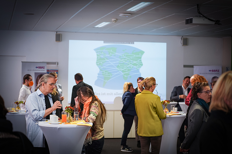 Einblick in ein Firmenfr&uuml;hst&uuml;ck. Personen stehen an Stehtischen und unterhalten sich